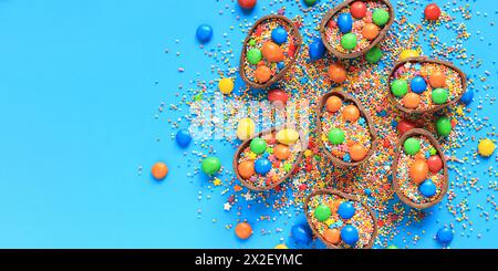 Oeufs en chocolat avec des bonbons et des saupoudres de couleur sucre sur un fond bleu, vue de dessus. Composition de Pâques. Des moitiés d'œufs en chocolat sur la table. Fes Banque D'Images