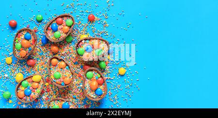 Oeufs en chocolat avec des bonbons et des saupoudres de couleur sucre sur un fond bleu, vue de dessus. Composition de Pâques. Des moitiés d'œufs en chocolat sur la table. Fes Banque D'Images