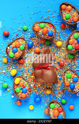 Lapin en chocolat et bonbons, saupoudres de sucre coloré sur un fond bleu, vue de dessus. Composition de Pâques. Lapin en chocolat de Pâques. Friandise festive. CH Banque D'Images