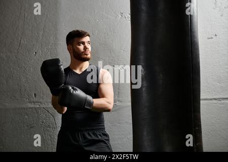 Un bel homme avec une barbe se tient à côté d'un sac de punching dans un gymnase, pratiquant la boxe. Banque D'Images