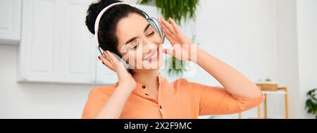 Une femme élégante dans une chemise orange aime la musique à travers des écouteurs. Banque D'Images