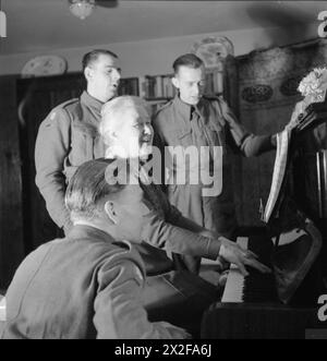 MRS BUGLER GOES TO WAR : EVERYDAY LIFE IN EAST DEAN, SUSSEX, ENGLAND, 1943 - après le thé, Mrs Bugler est assise au piano et conduit ses invités soldats (dont Harry Wardle (debout à gauche) et Harry Baddeley (debout à droite)) dans une chanson chantée Banque D'Images