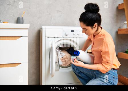 Une femme élégante verse de l'eau dans une machine à laver dans sa maison branchée pour nettoyer les vêtements. Banque D'Images