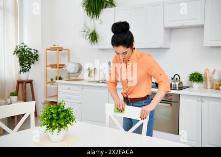 Une femme élégante en tenue décontractée se tient dans la cuisine, coupant habilement un morceau de papier avec précision et créativité. Banque D'Images