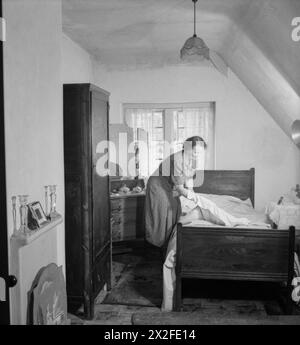 LES CHALETS DE FREEFOLK : LA VIE DANS LE VILLAGE DE FREEFOLK, HAMPSHIRE, ANGLETERRE, Royaume-Uni, 1943 - Mme Shadwell change le linge de lit dans l'une des chambres de sa maison dans le village de Freefolk dans le Hampshire. Chacun des salons et des chambres de ces maisons a une «cheminée carrelée moderne» (vue ici à gauche de la photo) et un éclairage électrique est installé dans toute la maison Banque D'Images