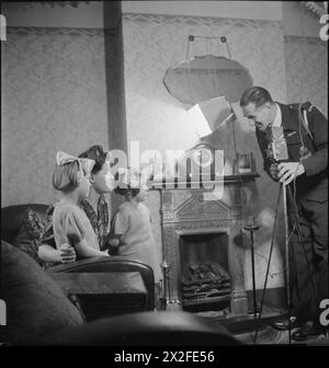 YMCA SNAPSHOTS FROM HOME : CIVILIAN PHOTOGRAPHERS AT WORK, UK, 1944 - un travailleur de la Défense civile, M. A E Moat, se prépare à photographier Mme F l White et ses filles Patricia (5 ans) et Doreen (4 ans) dans le salon de leur maison à Edmonton, pour envoyer au mari de Mme White, servir au moyen-Orient. M. Moat a installé une lumière électrique qui est clairement visible entre le miroir au-dessus de la cheminée et l'horloge. Une petite photographie de Trooper White est également visible sur la cheminée Banque D'Images