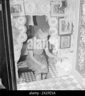 BRITISH CANALS IN WARTIME : TRANSPORT IN BRITAIN, 1944 - Une mère installe son bébé pour dormir dans la cabine de son bateau de canal. La cabine est ornée de plaques décoratives, de photographies de famille et de dentelle, qui, selon la légende originale «sont les caractéristiques d'une bonne cabine de bateau de canal» Banque D'Images