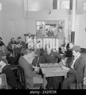 LONDON MERCHANT SEAMEN'S HOME AND RED ENSIGN CLUB, 1942 - George Lappin (troisième en partant de la gauche, lisant un magazine) et d'autres marins marchands se détendent dans le salon moderne du Merchant Seamen's Home and Red Ensign Club. Le salon est équipé d'un café-bar, qui peut être vu en arrière-plan, un ouvrier de cantine fournissant deux marins marchands avec du thé. Le reste des hommes lisent ou jouent aux dominos de la marine marchande Banque D'Images