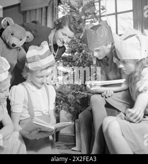 FÊTE DE NOËL POUR LA FILLE du SOLDAT DEVEREUX : NOËL EN TEMPS DE GUERRE, PINNER, MIDDLESEX, DÉCEMBRE 1944 - Jean Devereux, douze ans, lit un livre qu'elle a reçu comme cadeau de Noël chez elle à Pinner, sous le regard de sa mère et de plusieurs de ses amis. Un grand ours en peluche peut être vu à gauche de la photo. La légende originale indique que cela dans un vieil ours en temps de paix, et n'était pas un cadeau de Noël, car de tels jouets ne sont plus disponibles. Derrière eux, on peut voir le sapin de Noël est un cadeau du mari de Mme Devereux, qui sert actuellement dans l'armée outre-mer. L'arbre a été acheté Banque D'Images