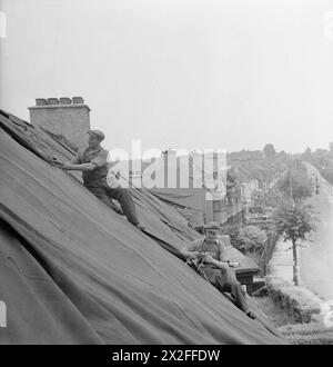 CAMP DE LONDRES DE L'ÉQUIPE DE RÉPARATION BLITZ : LA VIE QUOTIDIENNE AVEC LES ÉQUIPES DE RÉPARATION BLITZ, LONDRES, ANGLETERRE, Royaume-Uni, 1944 - les constructeurs de l'équipe de réparation Blitz ont posé des bâches sur les toits des maisons pour protéger l'intérieur contre les éléments suite à une attaque V1, qui a endommagé la plupart des maisons dans la rue. Ces constructeurs font partie d'une grande équipe qui s'est rendue à Londres depuis diverses régions du pays pour aider à réparer ces dommages Banque D'Images