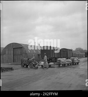 LA GRANDE-BRETAGNE APPROVISIONNE LE MAGASIN DE L'ARMÉE américaine : LES AMÉRICAINS EN GRANDE-BRETAGNE, 1943 - le soldat Herbert M Mack (du 208 Gadson Street, Ocala, Floride) conduit un petit camion tirant trois remorques contenant des sacs de café dans un magasin de l'armée américaine, quelque part en Grande-Bretagne. Un autre GI pousse une brouette de sac alors qu'il marche à côté du camion. Derrière eux, on peut voir les cabanes Romney au toit rond du camp et plusieurs wagons de marchandises, qui ont transporté des marchandises de toute la Grande-Bretagne au camp. Les marchandises arrivent par chemin de fer et par route Banque D'Images