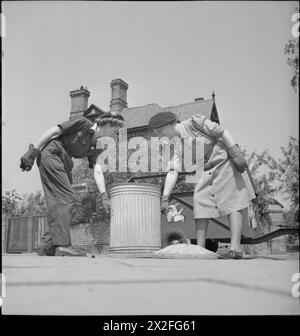 PIG FOOD : WOMEN'S VOLUNTARY SERVICE COLLECTE LES DÉCHETS DE CUISINE RÉCUPÉRÉS, EAST BARNET, HERTFORDSHIRE, ANGLETERRE, 1943 - Winifred Jordan (à gauche) et Kathleen Kent du WVS se préparent à soulever une grande poubelle de nourriture pour porcs dans une rue d'East Barnet, qu'ils vident dans leur remorque, juste visible derrière eux Banque D'Images