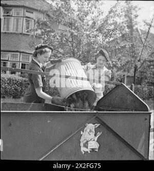 NOURRITURE POUR COCHONS : LE SERVICE VOLONTAIRE DES FEMMES COLLECTE LES DÉCHETS DE CUISINE RÉCUPÉRÉS, EAST BARNET, HERTFORDSHIRE, ANGLETERRE, 1943 - les travailleurs de récupération de WVS Winifred Jordan (à gauche) et Kathleen Kent vident le contenu d'une grande poubelle à cochons dans leur remorque. Ces restes de cuisine récupérés seront utilisés comme nourriture pour porcs, d’où la peinture d’un porc qui se prépare à manger sur le côté de la remorque Banque D'Images