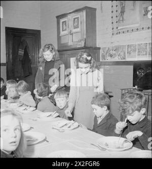 LES JARDINS DU VILLAGE NOURRISSENT LES ÉCOLIERS : PRODUCTION ALIMENTAIRE À KNIGHTON-ON-TEME, WORCESTERSHIRE, ANGLETERRE, Royaume-Uni, 1943 - les enfants de l'école du village à Knighton-on-Teme profitent de leur repas du midi dans une salle de classe qui sert de salle à manger. Chaque repas coûte 5 pence et chaque enfant achète cinq billets pour couvrir les repas de la semaine. Ici, nous voyons Sheila Abbott (à gauche) et Betty Halbeard ramasser les billets de repas des plus jeunes enfants Banque D'Images