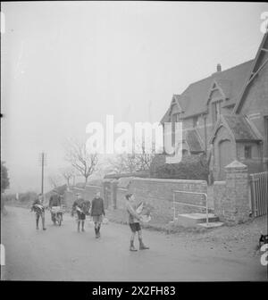 LES JARDINS DU VILLAGE NOURRISSENT LES ÉCOLIERS : PRODUCTION ALIMENTAIRE À KNIGHTON-ON-TEME, WORCESTERSHIRE, ANGLETERRE, Royaume-Uni, 1943 - Un groupe de garçons arrive à l'école avec des légumes pour le repas du midi. Derrière eux, sur la voie, alors qu'ils approchent du bâtiment de l'école, il y a un homme avec une brouette pleine de légumes. Tous les légumes ont été achetés aux membres de l'Association des produits du village Banque D'Images