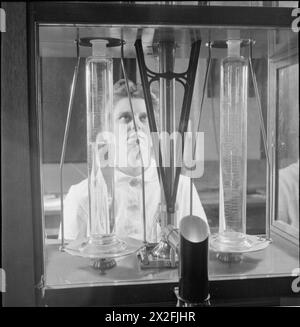 En 1944, au National Physical Laboratory de Teddington, Middlesex, une femme scientifique de la Division de métrologie teste la verrerie volumétrique en pesant de l'eau dans un cylindre gradué sur une balance sensible, illustrant les travaux scientifiques de guerre. Banque D'Images