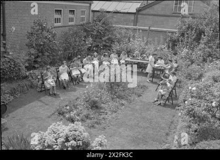 Une PHOTO D'Une VILLE DU SUD : LIFE IN WARTIME READING, BERKSHIRE, ANGLETERRE, Royaume-Uni, 1945 - les filles participent à un cours de tricot en plein air au soleil dans le jardin encastré de l'école secondaire moderne de Caversham. Il y a aussi deux filles qui travaillent sur des machines à coudre, assises aux tables qui ont été dressées sur l'herbe. Selon la légende originale, la tendance est de diviser les garçons et les filles à partir de 11 ans en écoles séparées ou en groupes séparés dans la même école. Banque D'Images