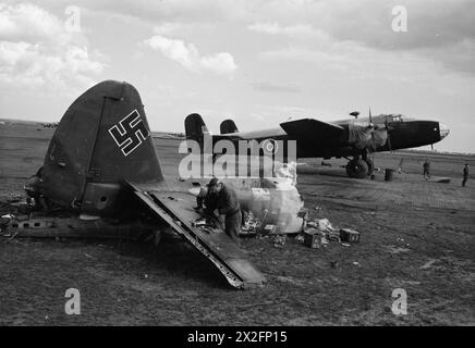 FORCE AÉRIENNE ROYALE : ITALIE, BALKANS ET EUROPE DU SUD-EST, 1944-1945. - L'équipe au sol utilise l'empennage d'une épave Junkers Ju 88 comme établi à Celone, en Italie. Handley page Halifax Mark II Series 1A, JN894 'y', du No. 614 Squadron RAF se trouve sur un dispersé recouvert de planches en acier percé (PSP) derrière Royal Air Force, Royal Air Force Regiment, Sqdn, 162 Banque D'Images