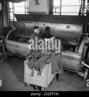 BLANCHISSERIE EN TEMPS DE GUERRE : LE TRAVAIL DE GLENIFFER BLANCHISSERIE, CATFORD, LONDRES, ANGLETERRE, ROYAUME-UNI, 1944 - Un ouvrier de Gleniffer Laundry charge des vêtements dans une grande machine de « nettoyage français ». La légende originale indique que la majorité des vêtements nécessitant un tel traitement sont des costumes et des pardessus Banque D'Images