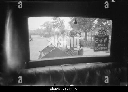 NOURRITURE POUR PORCS : LE SERVICE VOLONTAIRE DES FEMMES COLLECTE LES DÉCHETS DE CUISINE RÉCUPÉRÉS, EAST BARNET, HERTFORDSHIRE, ANGLETERRE, 1943 - Une vue à travers la fenêtre arrière de la voiture de l'unité de collecte de porcs WVS, alors que les membres de l'unité East Barnet vident un bac à porcs dans la remorque. De gauche à droite, ils sont : Kathleen Kent (chef de l'unité), Mlle Winifred Jordan (à l'arrière de la caméra) et Mme Gerald de Rivaz Banque D'Images