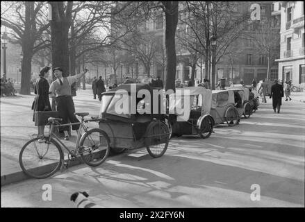 TRAFIC PARISIEN, PRINTEMPS 1945 : LA VIE QUOTIDIENNE À PARIS, FRANCE, 1945 - Une vue d'ensemble d'un rang de taxi : à la française! Une rangée de taxis Velo bordent le trottoir d'une rue verdoyante sous le soleil printanier, quelque part à Paris. Les piétons peuvent être clairement vus, vaquant à leurs activités quotidiennes Banque D'Images