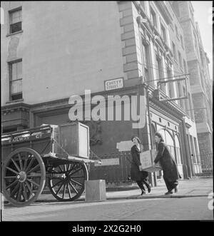 VAN GIRL : LIVRAISONS DE CHEVAUX ET DE CHARRETTES POUR LES CHEMINS DE FER LONDONIENS, MIDLAND ET ÉCOSSAIS, LONDRES, ANGLETERRE, 1943 - après le déjeuner, Lilian Carpenter (à gauche) et Vera Perkins ramassent des objets à charger dans leur fourgon tiré par des chevaux et à les ramener au dépôt pour le transport en train. Ils sont sur le point de charger un coffre à thé, récupéré dans un bâtiment au coin de la rue Chitty, sur la camionnette de la LMS Railway Company. Un petit chat est juste visible derrière Lilian, regardant la procédure de derrière les balustrades Banque D'Images