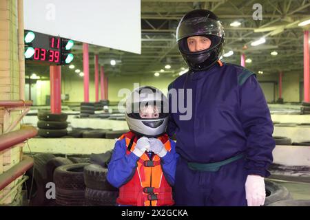 le petit garçon et son entraîneur de karting sont debout dans des casques ; sol pour le karting Banque D'Images