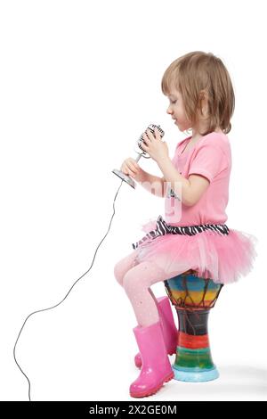 Petite fille en fille dans une robe rose et dans un gumboots rose s'assoit sur le djembé et chante dans le microphone. Banque D'Images