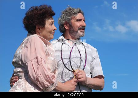 vieil homme et femme embrassant, tenant des raquettes de badminton, ciel bleu Banque D'Images