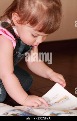 belle petite fille en combinaison denim et chemise rose lit livre Banque D'Images