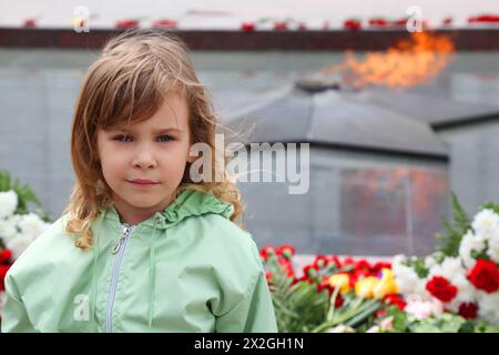 belle petite fille se tient près du mémorial, flamme éternelle, fleurs Banque D'Images