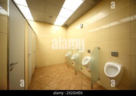 urinoirs et portes dans les toilettes publiques, carreaux jaunes sur le sol et les murs Banque D'Images