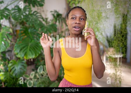 Femme noire intéressée prend pause pour discuter smartphone ont une conversation agréable surround par les plantes. Banque D'Images