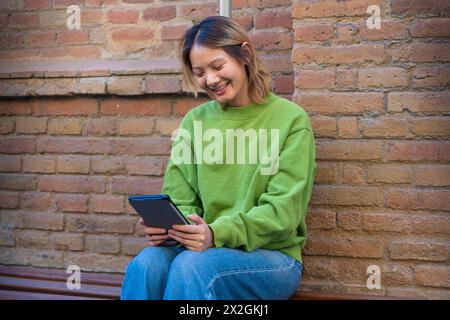 Jeune femme asiatique souriante assise surfant sur Internet sur une tablette numérique. Banque D'Images