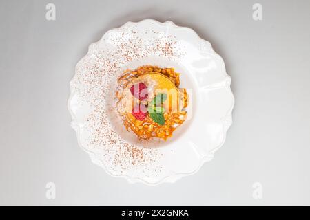 Crêpes moelleuses avec des framboises et des feuilles de menthe sur une plaque blanche sur un fond blanc propre. Gros plan. Banque D'Images