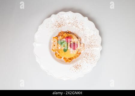 Crêpes moelleuses avec des framboises et des feuilles de menthe sur une plaque blanche sur un fond blanc propre. Gros plan. Banque D'Images