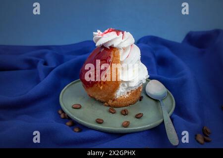 Gâteau Savarin avec glaçage rouge et crème fouettée sur tissu bleu Banque D'Images