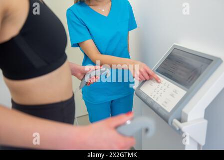 Un praticien de la santé assiste une femme avec un test de composition corporelle à l'aide d'un équipement de pointe. Banque D'Images