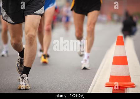 Les jambes de l'homme de course dans des shorts de sport et des chaussures de jogging près du cône de couleur sur l'asphalte Banque D'Images