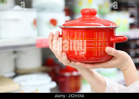 les mains de la femme tiennent le pot rouge en magasin, l'hôtesse choisit des plats pour la cuisine ; faible profondeur de champ Banque D'Images