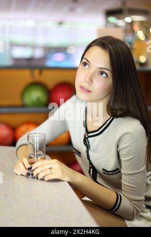 Belle femme brune est assise à table et tient le verre avec de l'eau pure dans le bowling ; faible profondeur de champ Banque D'Images