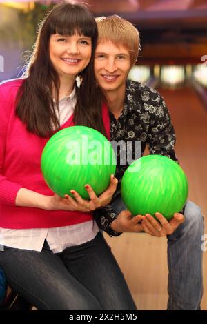 jeune femme souriante et mari avec des balles vertes assis dans le club de bowling Banque D'Images