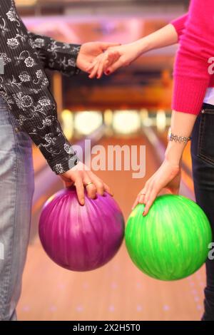 Mains féminines et masculines avec des balles dans le club de bowling ; homme et femme tenant la main Banque D'Images