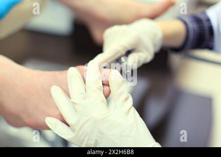 Mains de femme portant des gants en caoutchouc pratiquant la chiropodie en prenant soin des pieds masculins Banque D'Images