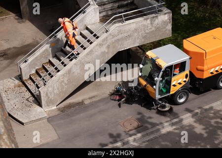 Bâle, Suisse - 18 avril 2024 : travailleur portant un uniforme orange nettoyant les escaliers de pont de la ville avec souffleur de feuilles et un balayeur de rue nettoyant le véhicule Banque D'Images