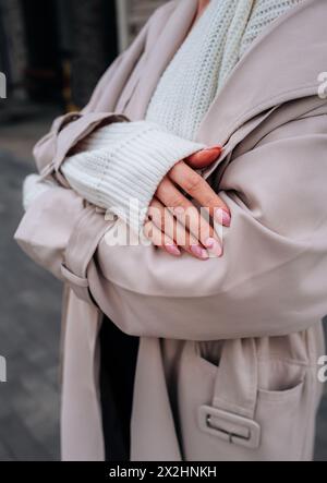 Détails de mode en tissu de style urbain d'un pull blanc tricoté et trench-coat beige pour femmes. Mode urbaine contemporaine Banque D'Images