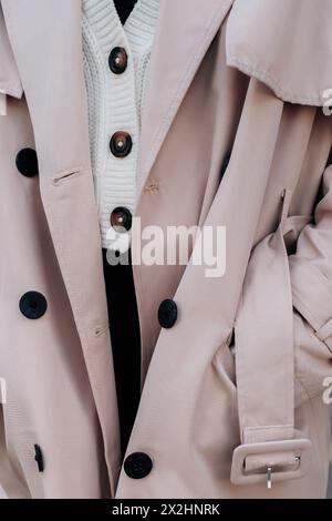 Gros plan sur les détails de mode d'un pull boutonné blanc tricoté et un trench beige pour femme. Mode urbaine contemporaine Banque D'Images