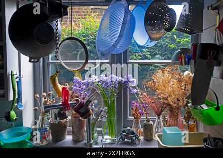 Ustensiles de cuisine passoire suspendue au-dessus de l'évier par les plantes de fenêtre bluebells dans des vases à l'intérieur de la maison maison mitoyenne à Londres Angleterre KATHY DEWITT Banque D'Images