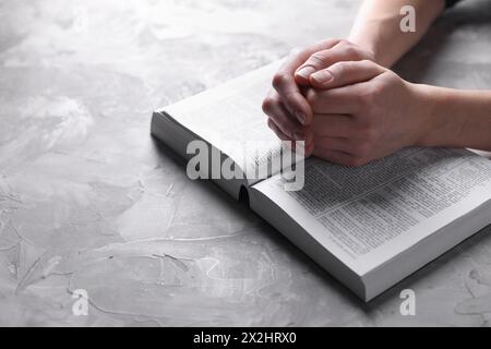 Religion. Femme chrétienne priant sur la Bible à la table texturée grise, gros plan. Espace pour le texte Banque D'Images