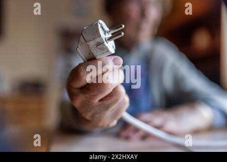 Personne âgée tenant un câble d'alimentation avec prise dans la main à la maison, symbolisant les coûts de l'énergie et la pauvreté, Cologne, Rhénanie du Nord-Westphalie, Allemagne Banque D'Images